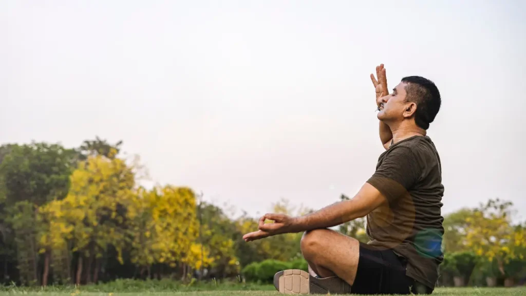 a person sitting on the grass in the middle of a field एण्ड doing Anulom Vilom yoga